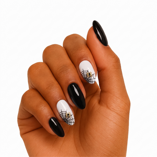 Black and white gel nail wraps with spiderweb print and gold spider charm accents.