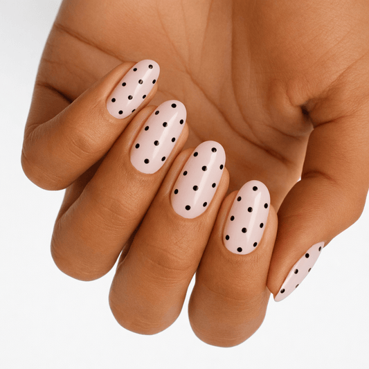 Hand displaying white nail wraps with black polka dot pattern for classic manicure