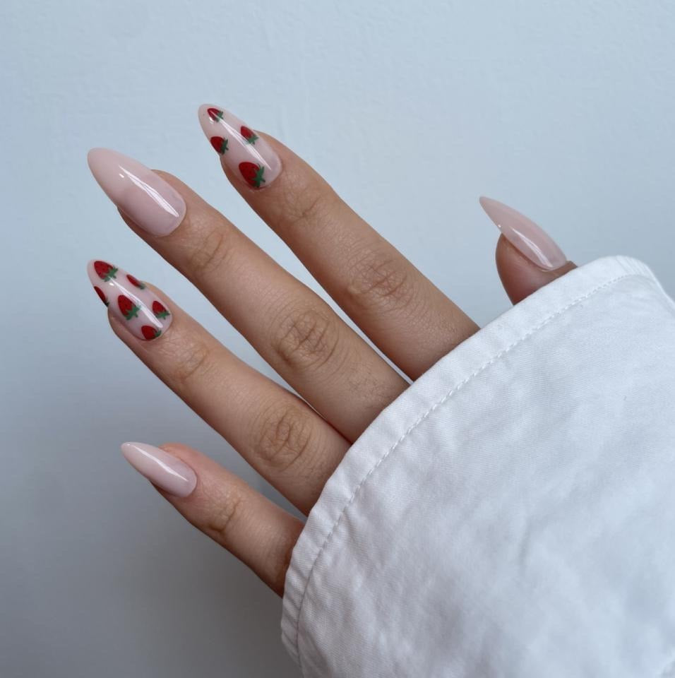 Glossy nude almond press-on nails with sheer strawberry fruit accent designs.