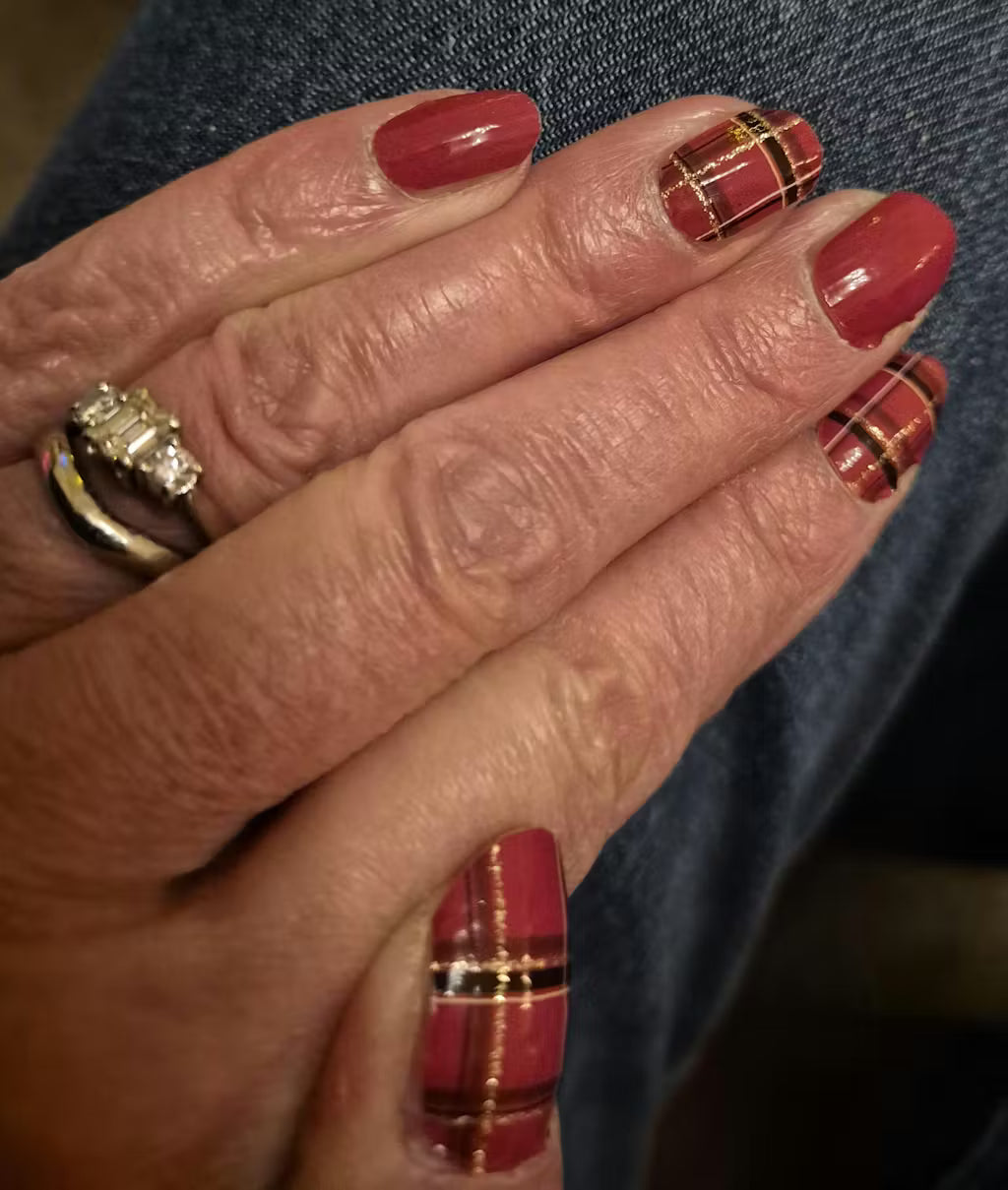 Red tartan plaid nail wraps on hand with gold accent lines festive manicure