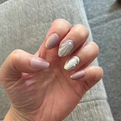 Nude press-ons with gold outlines, a shimmering shell accent and pearl detail