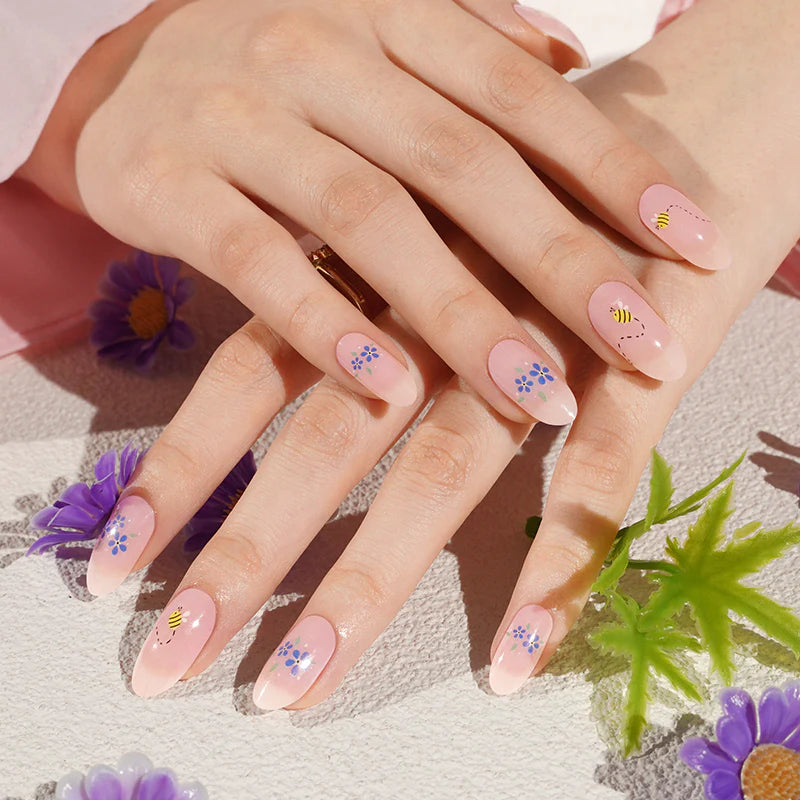 Sheer pink semi-cured gel wraps with blue flowers and bee design on almond nails