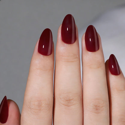 Short almond press-on nails in glossy deep burgundy with a jelly-like translucent finish