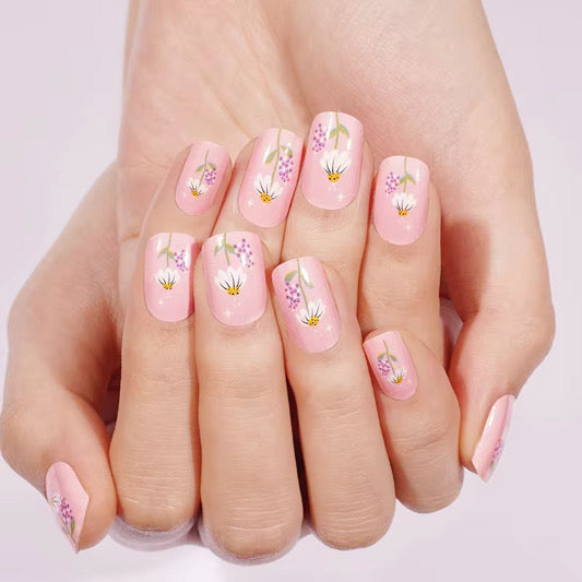Pink nail wraps with white daisy florals, purple blossoms, and sparkle accents
