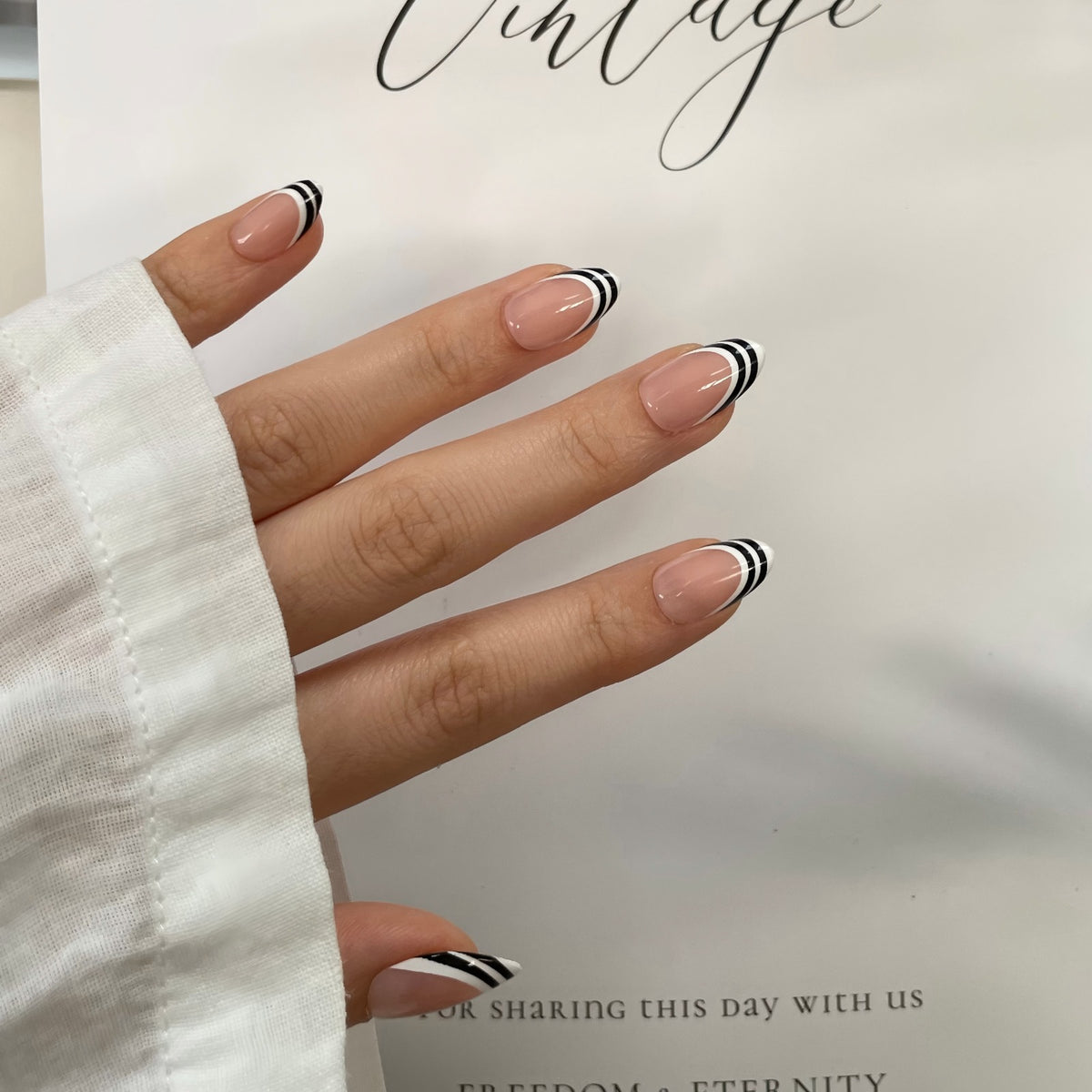 Short almond press-on nails, nude base with glossy black and white striped French tips