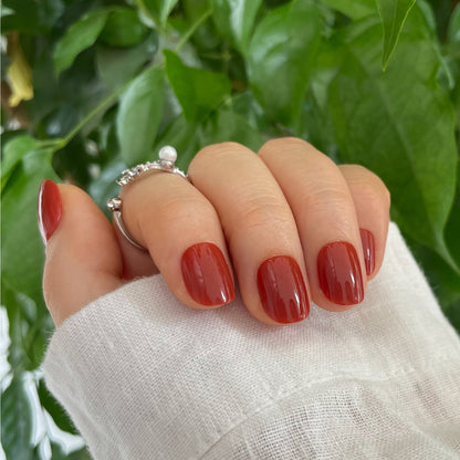 Extra short, round soft gel press-on nails in glossy brick red-orange shade