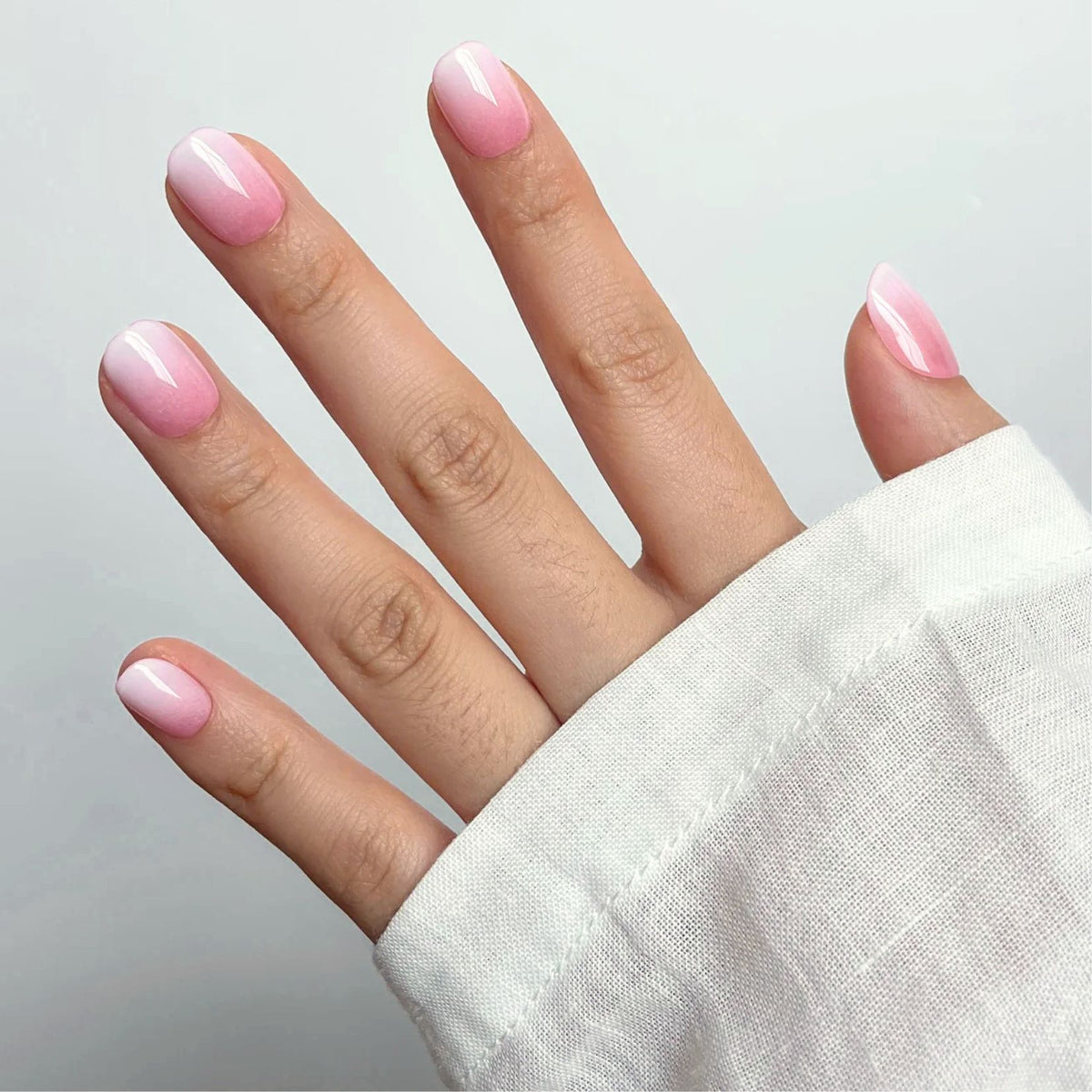 Soft gel press-ons in glossy pink-to-white ombré, extra short round nails