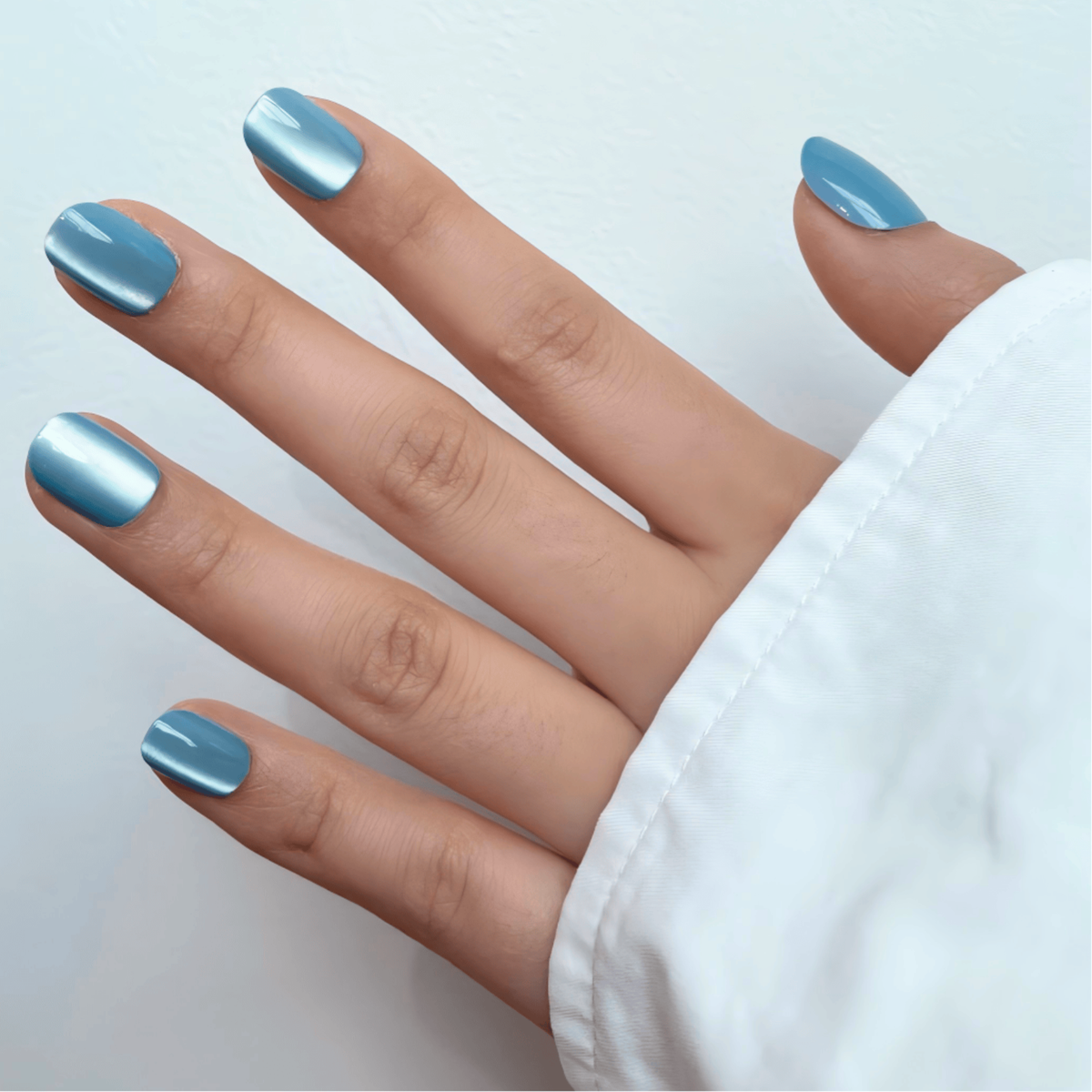 Short natural press-on nails in dusty blue with a glossy cat's eye shimmer finish