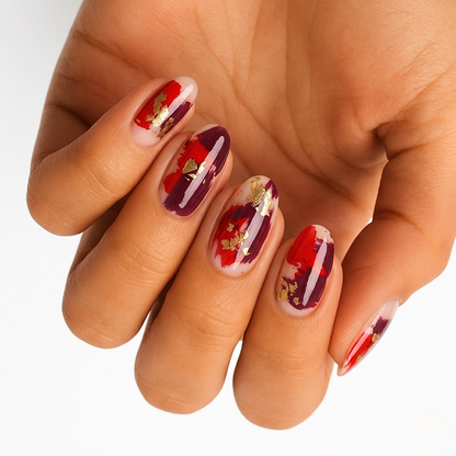 Nail wraps with red and burgundy brushstroke design, gold foil flecks on sheer nude base