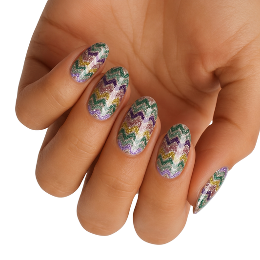 Glittery nail wraps with purple, green, and gold zigzag chevron pattern on almond nails