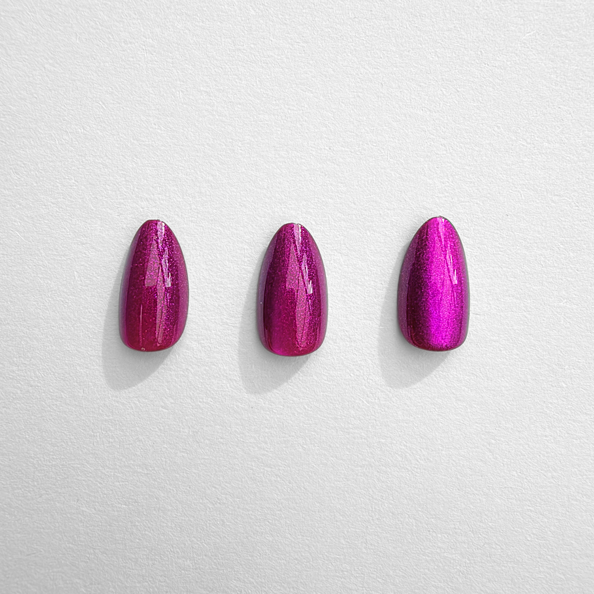 Three short almond soft gel press-on nails in magenta-pink with shimmering cat's eye finish.
