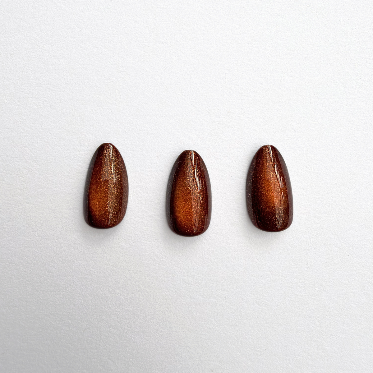 Short almond soft gel press-ons in glossy toffee-brown with cat's-eye shimmer effect.