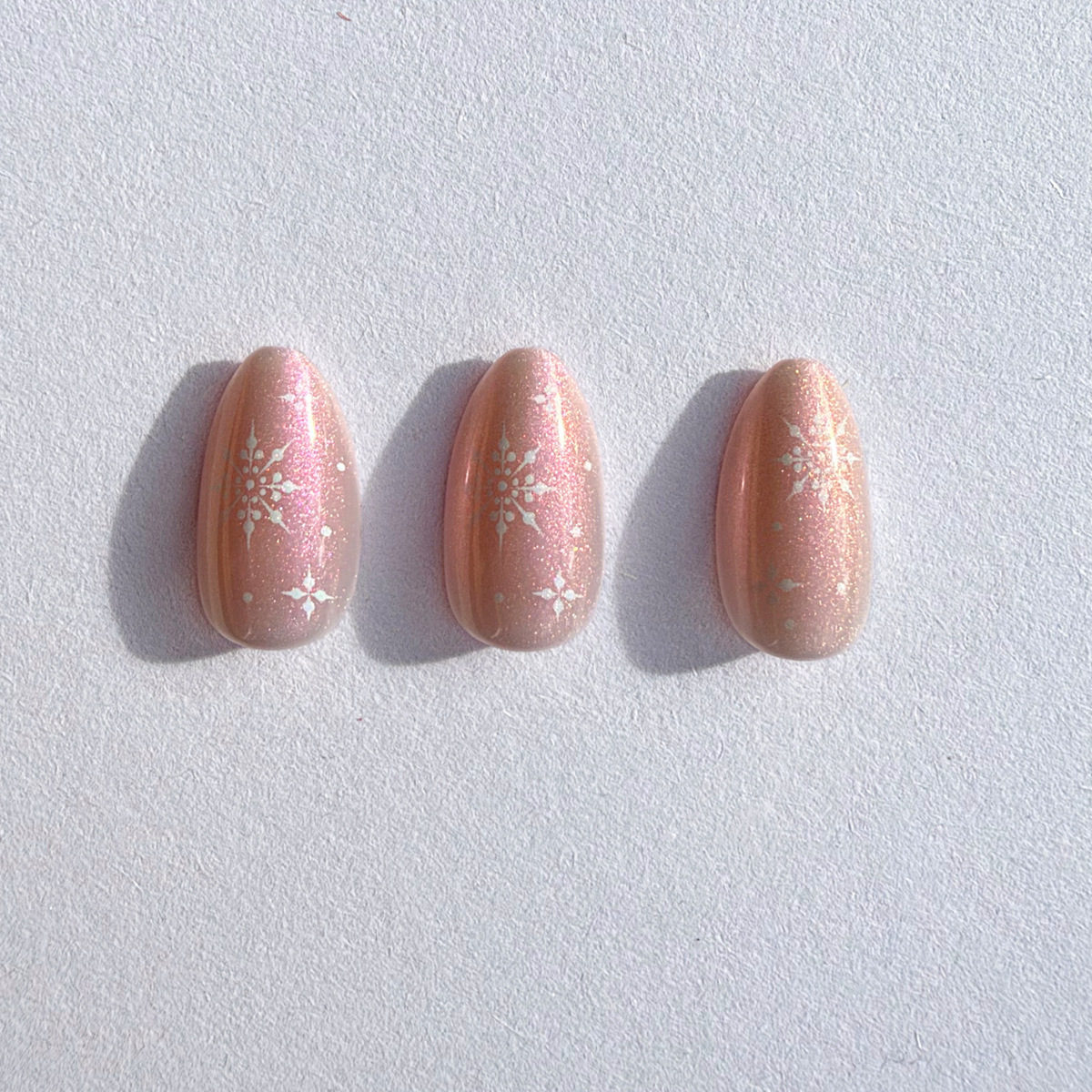 Soft gel press-on nails in shimmering peach-pink pearl finish with white snowflake accents