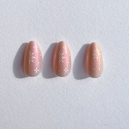 Soft gel press-on nails in shimmering peach-pink pearl finish with white snowflake accents