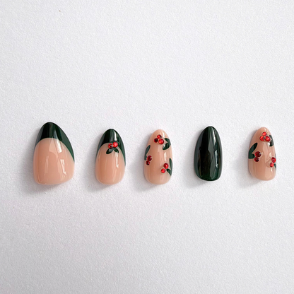 Nude and dark green press-on nails with holly leaf accents and red berry gems