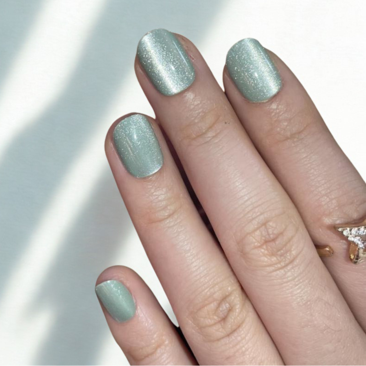 Sage green soft gel press-on nails with shimmering cat's eye magnetic finish, short round shape.