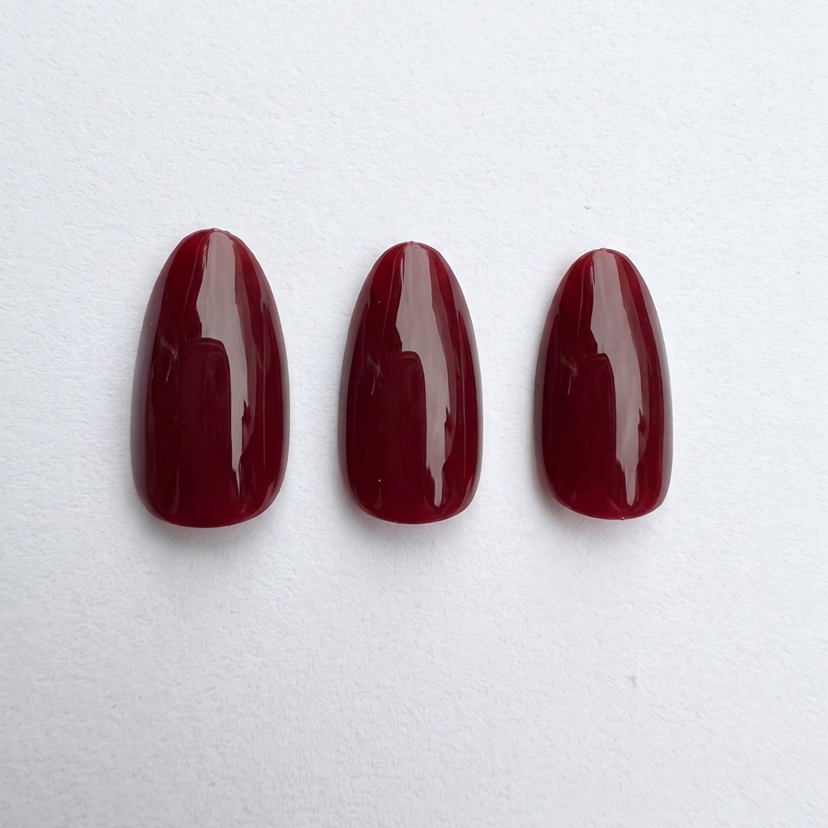 Short almond soft gel press-on nails in glossy deep dark red, Black Cherry shade.