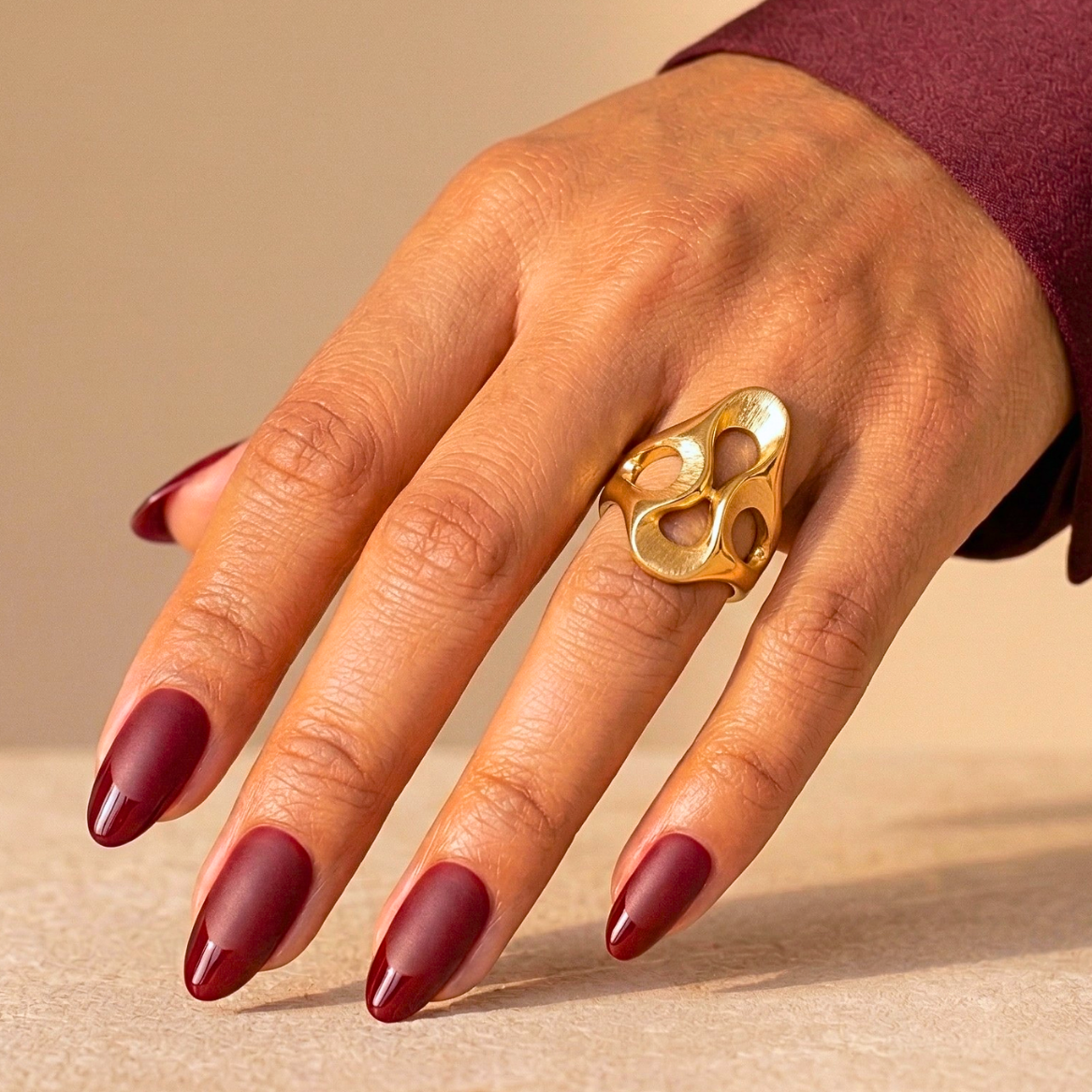 Burgundy red French manicure press-on nails in short almond shape on hand with gold ring
