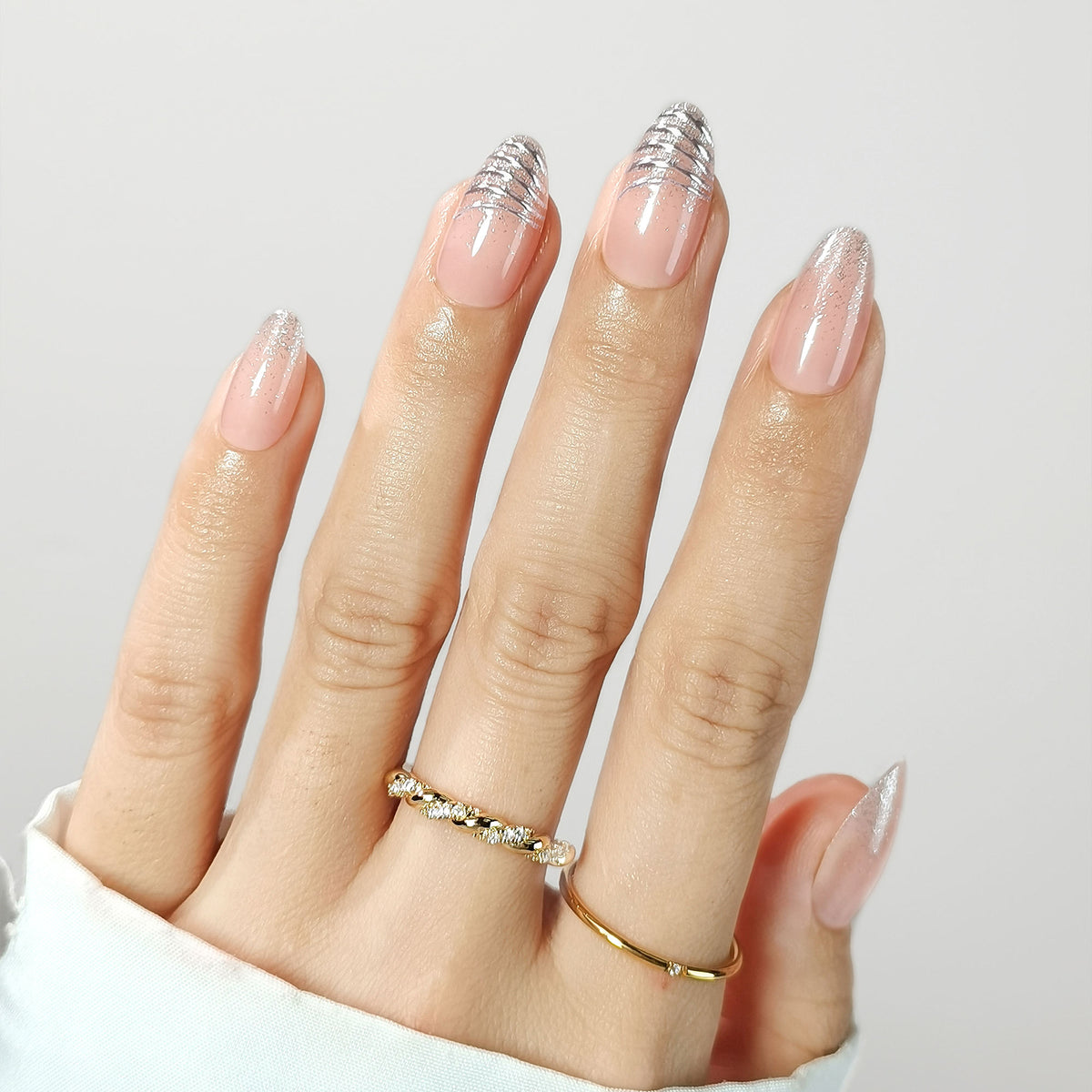 Sheer nude press-on nails with silver glitter French tips and shimmer accents, almond shape