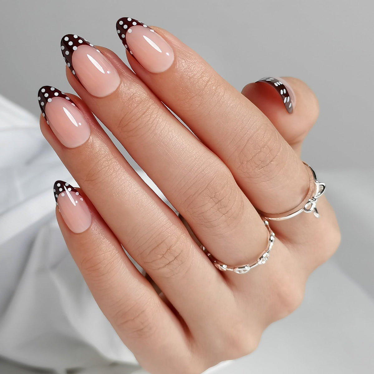 Glossy nude press-on nails with black polka dot French tips, almond shape
