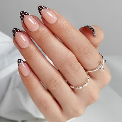 Glossy nude press-on nails with black polka dot French tips, almond shape