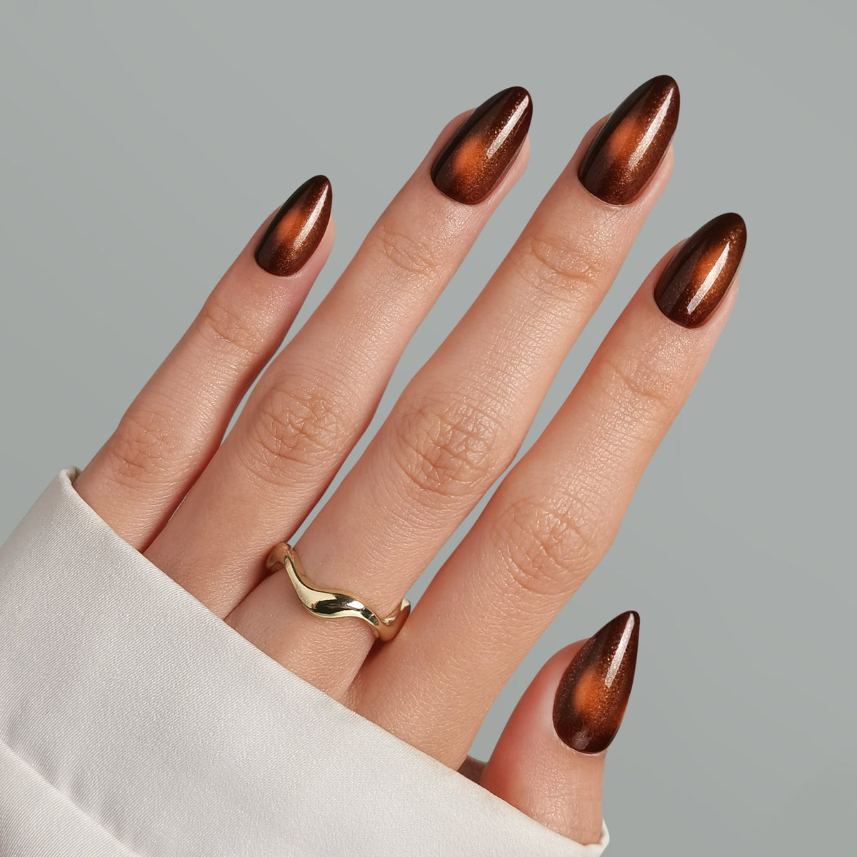 Almond press-on nails in deep brown with copper cat-eye shimmer, glossy finish.
