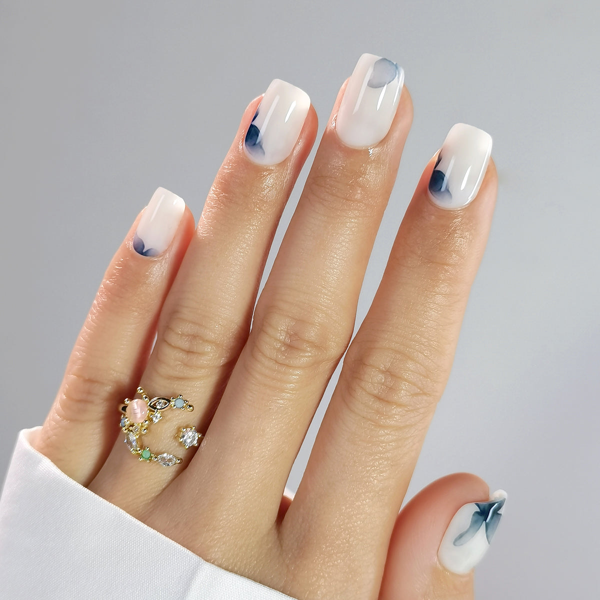 Sheer milky white press-on nails with abstract blue watercolor floral accents, glossy finish