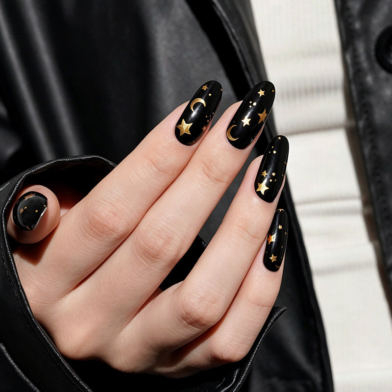 Black glossy nail wraps with gold star and moon celestial design on almond nails