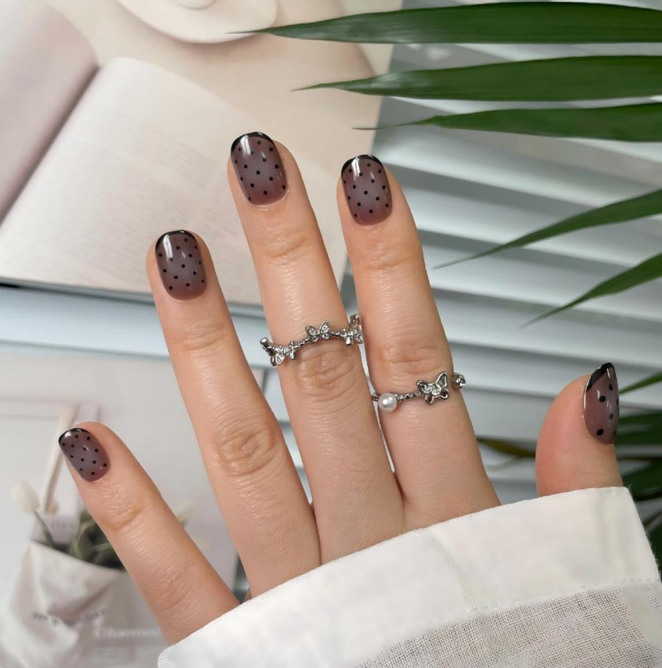 Sheer brown press-on nails with black polka dots and glossy French tips, short square shape