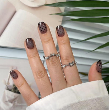 Sheer brown press-on nails with black polka dots and glossy French tips, short square shape