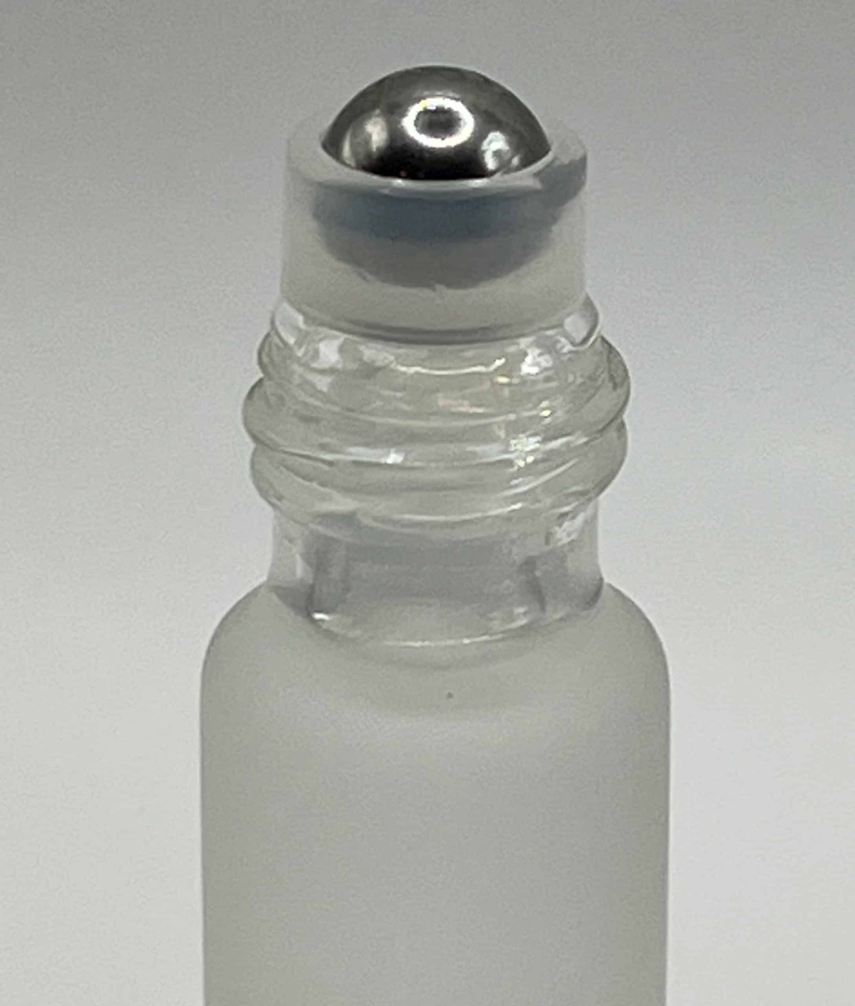 Close-up of frosted glass cuticle oil rollerball applicator with silver cap