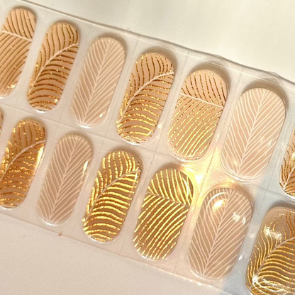 Nude gel nail wraps with gold feather pattern and geometric designs for elegant manicure