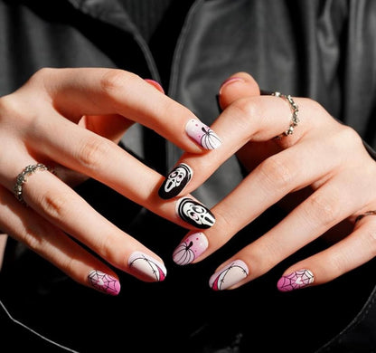 Halloween nail wraps on hand featuring pink spider webs, black ghosts, glow-in-the-dark spooky designs