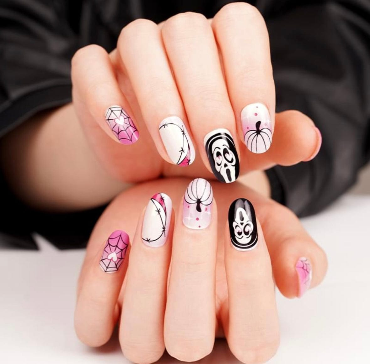 Pink and white Halloween nail wraps with spiderwebs, ghost face and pumpkin motifs, glow-in-the-dark.