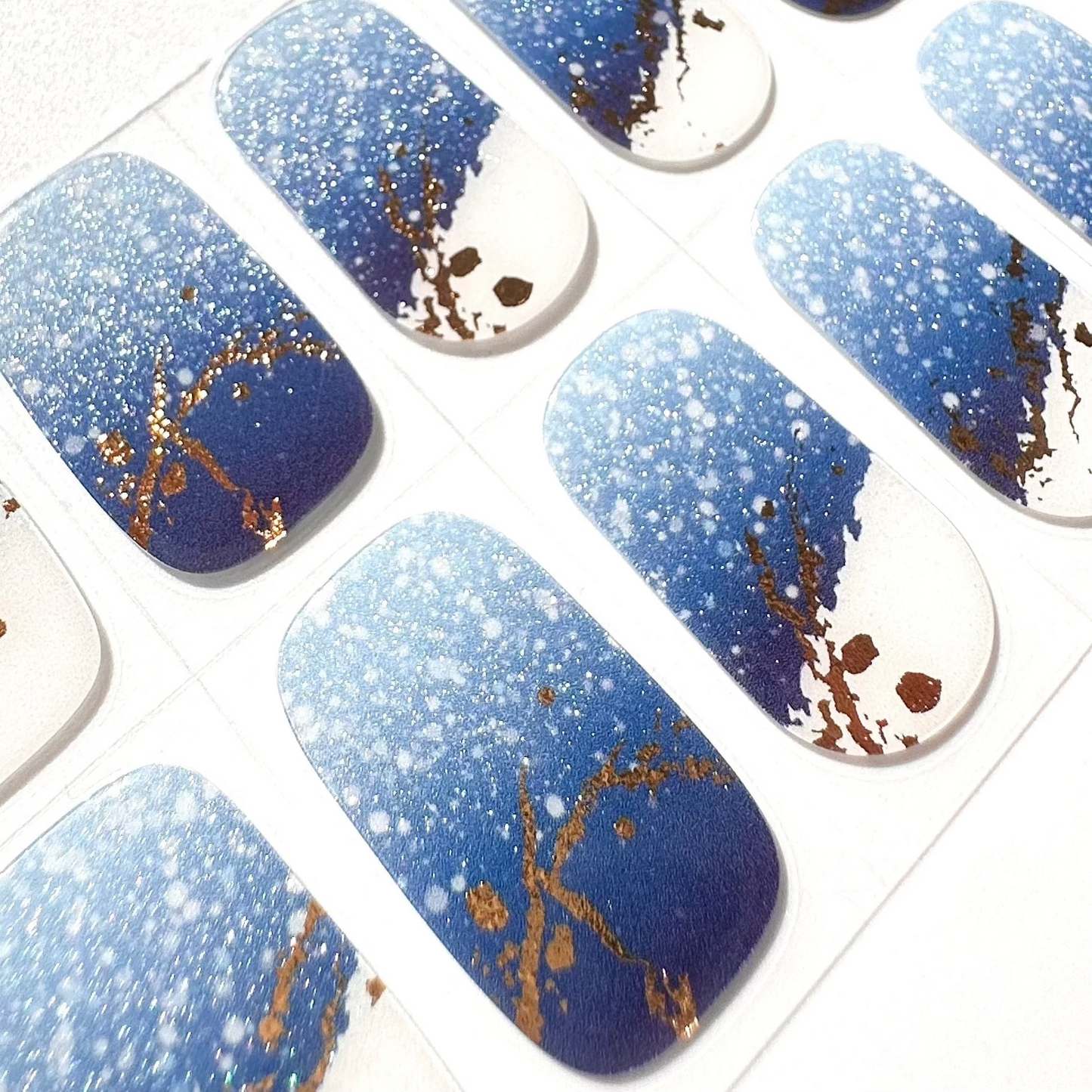 Blue gel nail wraps with white glitter spots and gold marble veining on clear backing sheet