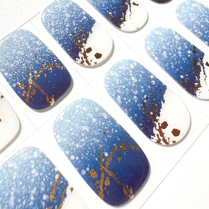 Blue gel nail wraps with white glitter spots and gold marble veining on clear backing sheet