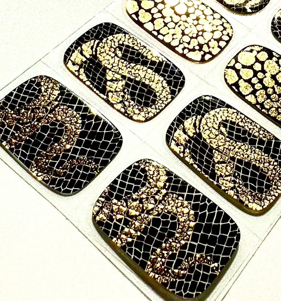 Close-up of black gel nail wraps featuring gold textured snake skin and mesh designs