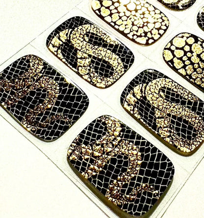 Close-up of black gel nail wraps featuring gold textured snake skin and mesh designs