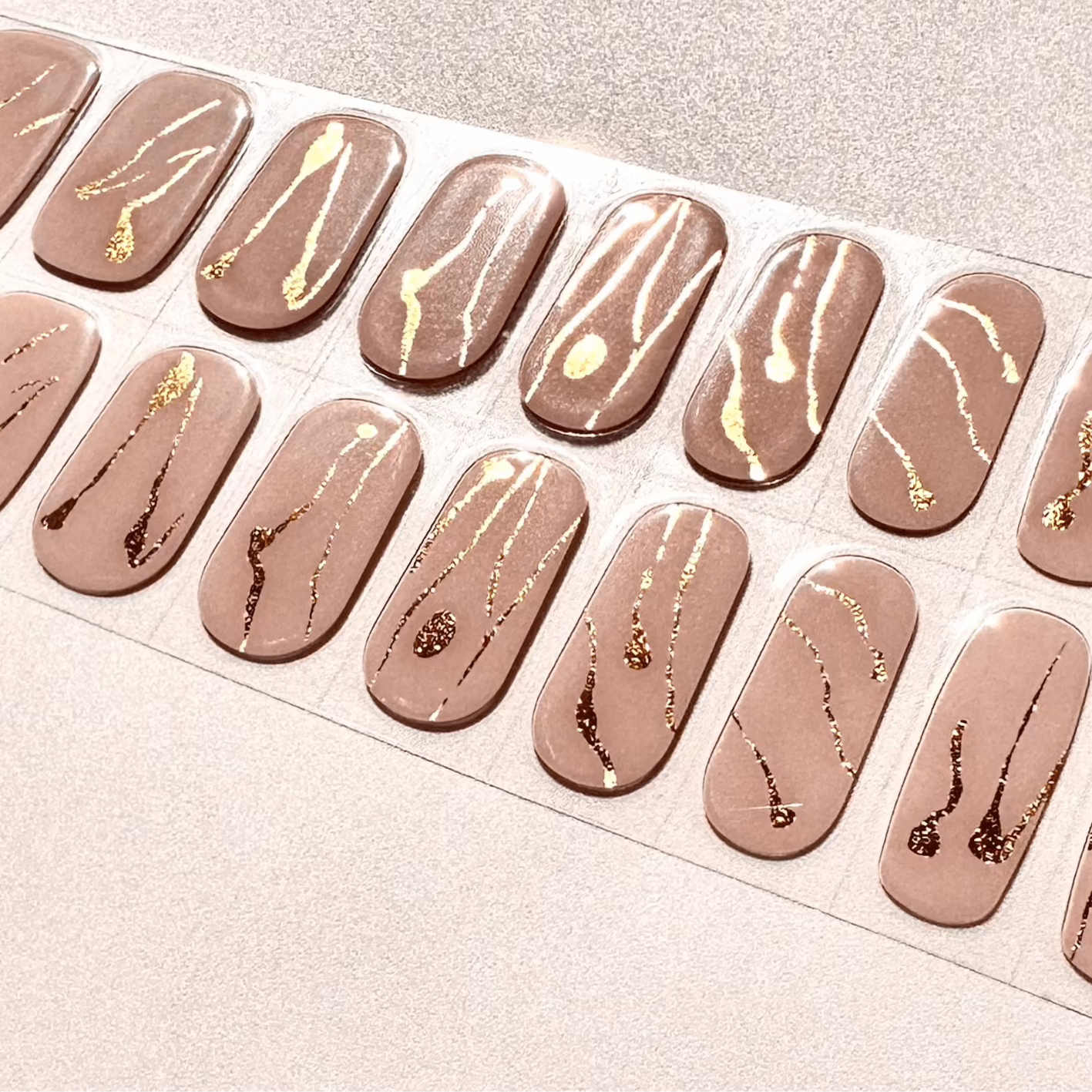 Nude gel nail wraps with gold foil marble patterns for elegant at-home manicures
