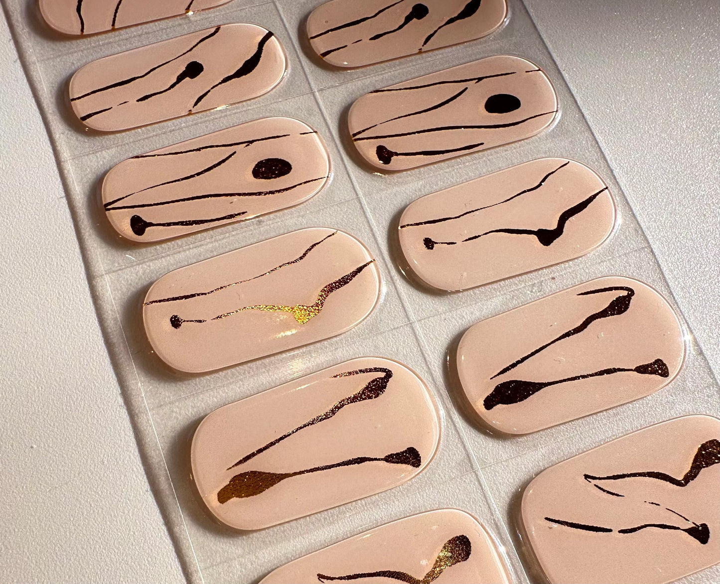 Individual nude gel nail wraps showing detailed marble patterns with gold foil accents