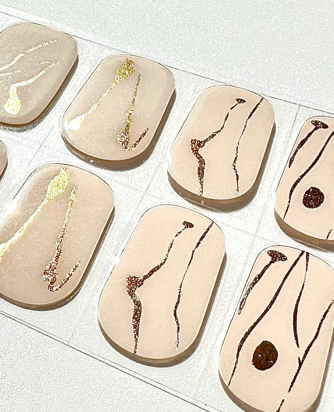 Close-up of nude gel nail wraps with metallic gold and brown marble effect patterns