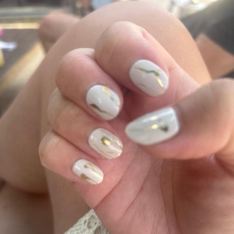 White gel nail wraps with gold foil accents on hand displaying elegant minimalist nail art