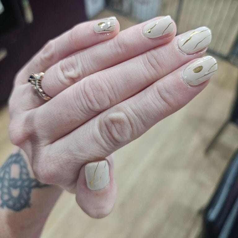 Hand wearing nude gel nails with gold marble patterns showing finished manicure look