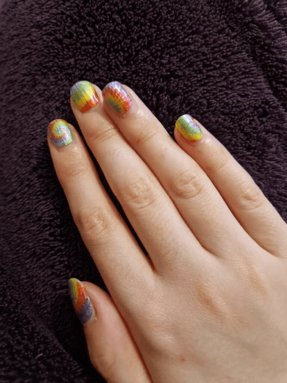 Hand wearing vibrant tie-dye spiral nail wraps in rainbow colours for kids