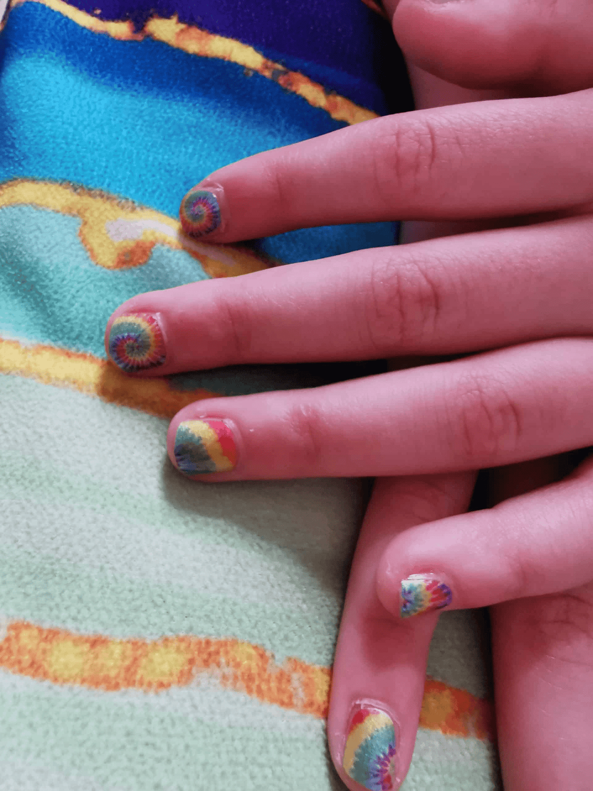 Close-up of child's hand with psychedelic rainbow tie-dye nail wraps applied