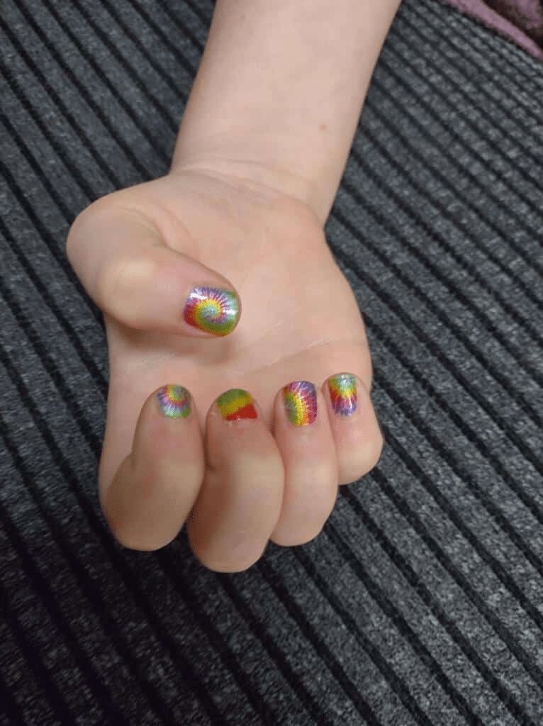 Child's hand showing colourful tie-dye psychedelic kids nail wraps with rainbow swirl patterns