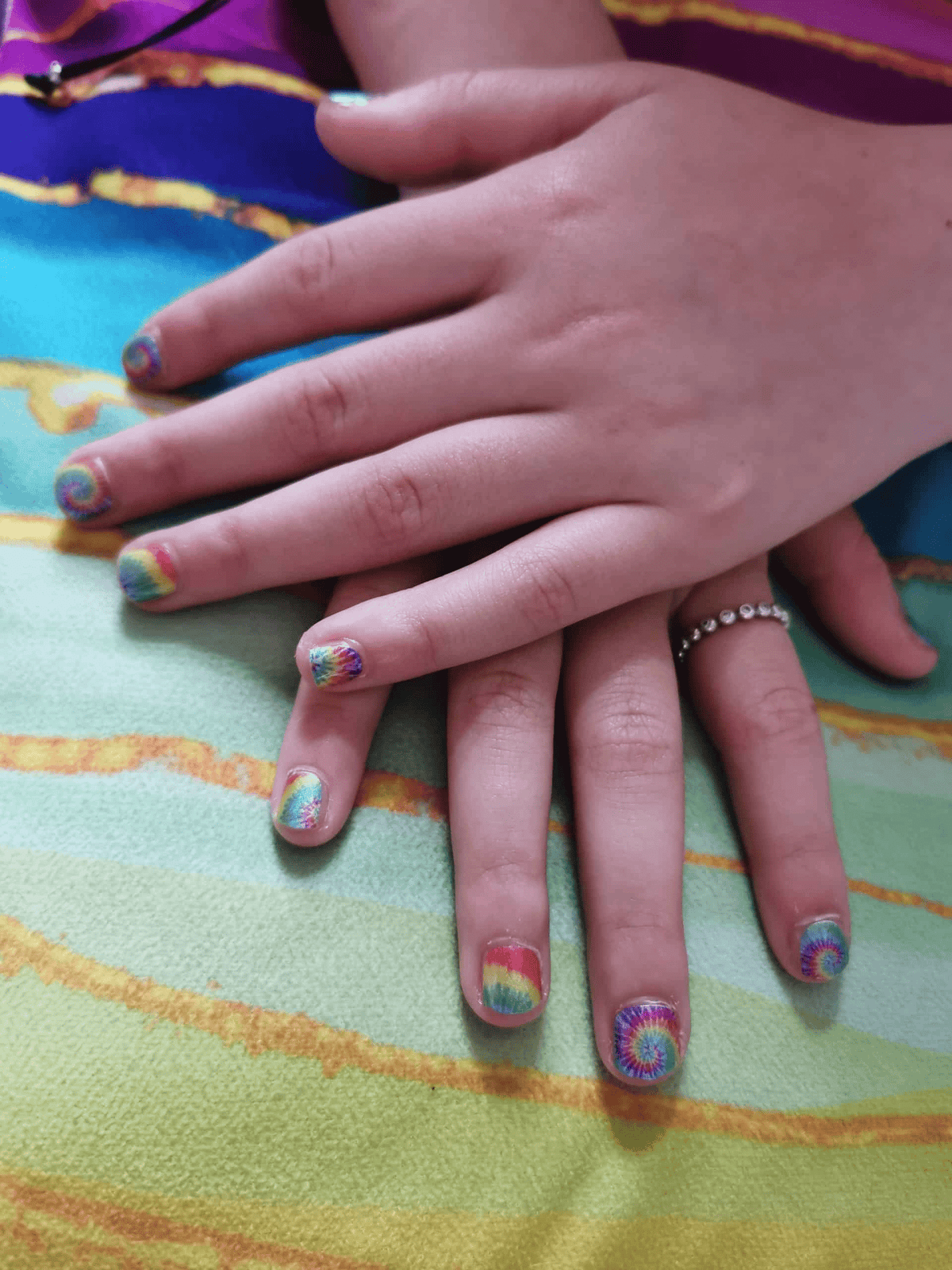 Two children's hands displaying vibrant tie-dye kids nail wraps with retro rainbow swirl designs