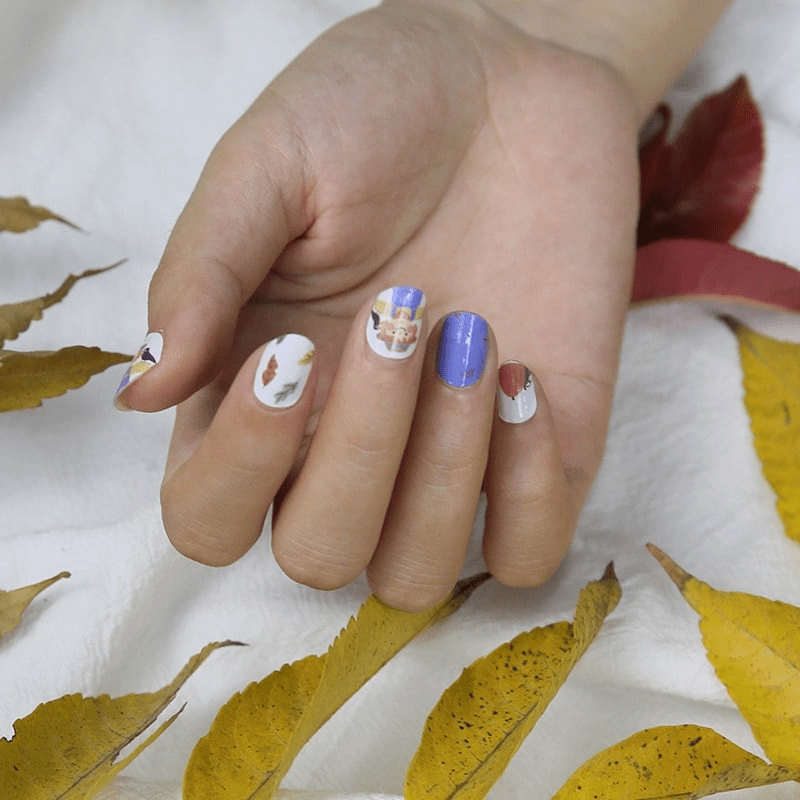 Child's hand wearing blue and white autumn nail art wraps with scarecrow character design