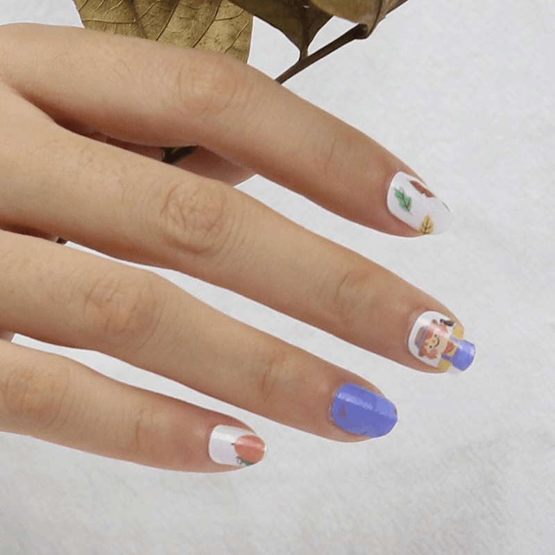 Children's autumn nail wraps on hand featuring blue, orange pumpkin and character designs