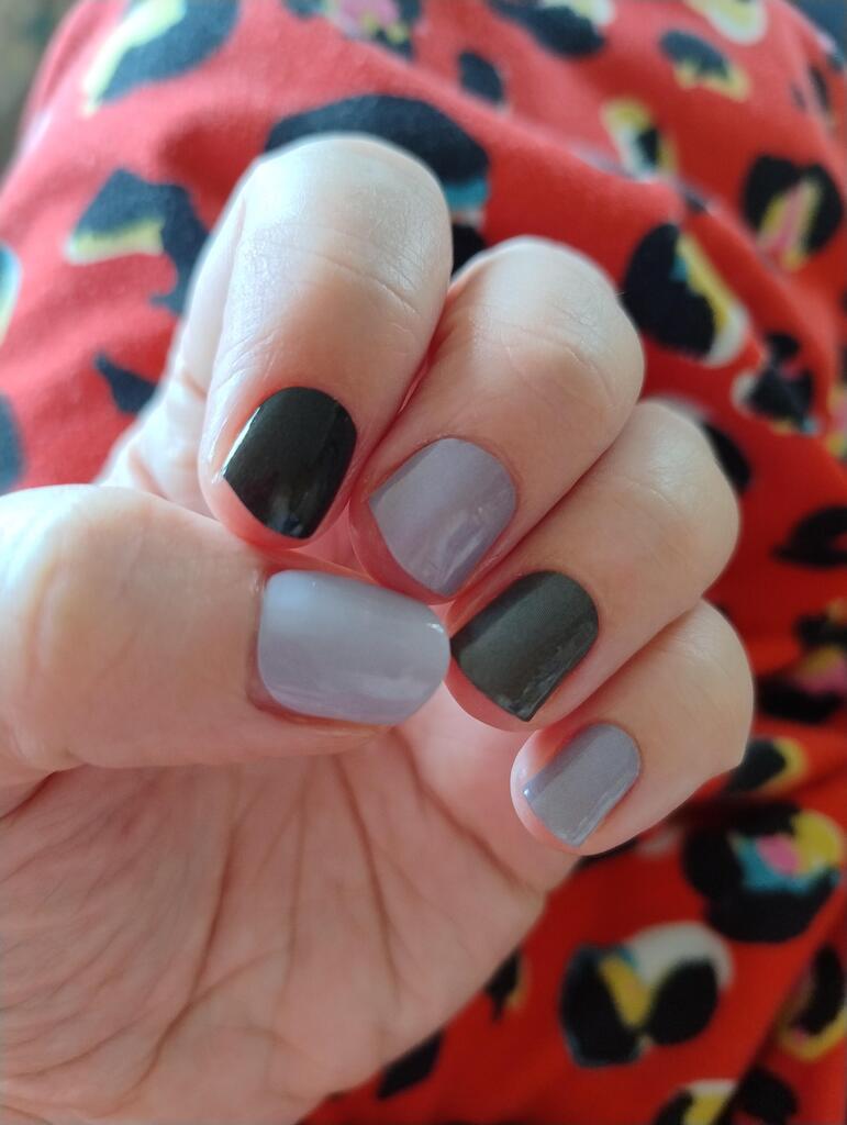 Hand displaying grey and black nail wraps in alternating pattern for at-home manicure